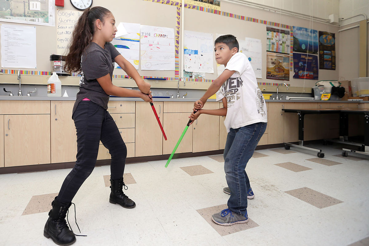 Two children play with toy lightsabers in a classroom