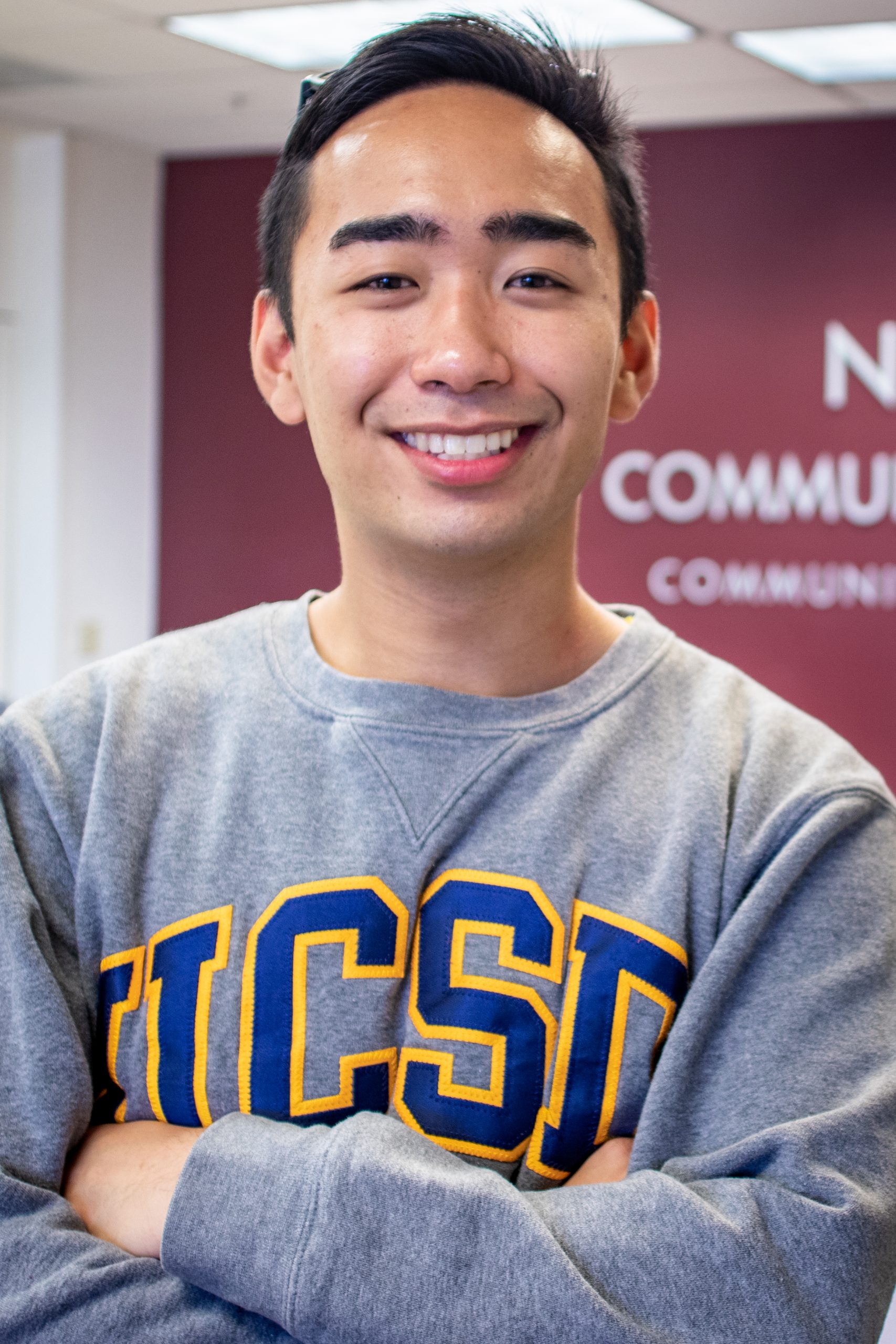 Eric De Castro, a young man with short dark hair smiles at the camera wearing a UCSD sweatshirt.