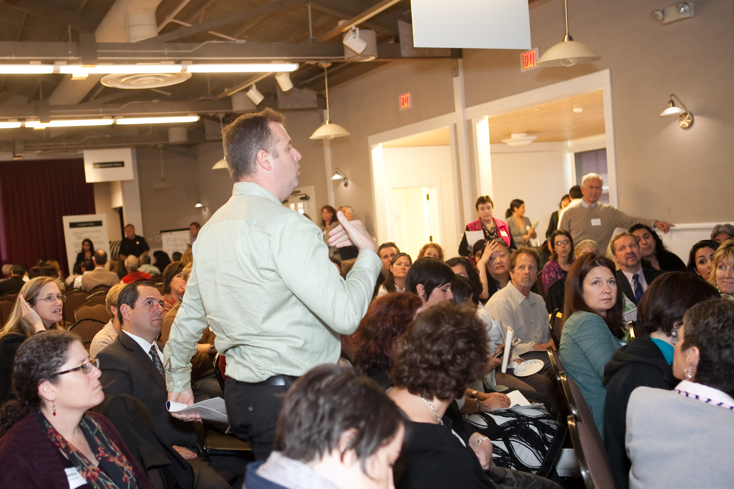 Speaker at Immigration Initiative Event, a white man wearing a long sleeve green dress shirt; the audience surrounds him.