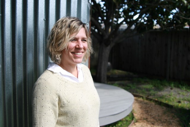 Alissa Abdo, a white woman with short blonde hair, smiles, wearing a pale yellow sweater over a white collared shirt.