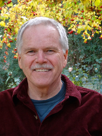 A photo of Ed Harrington, an older white man with short silver hair, wearing a blue shirt underneath a maroon quarter zip sweatshirt