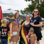 A family wearing festive rainbow clothing smiles for a photo.