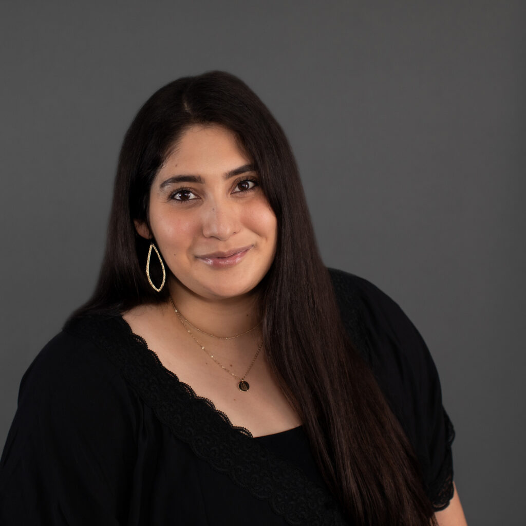 Luz Casillas-Del Rosario, a Latina woman with long dark hair, smiles at the camera wearing a black shirt.