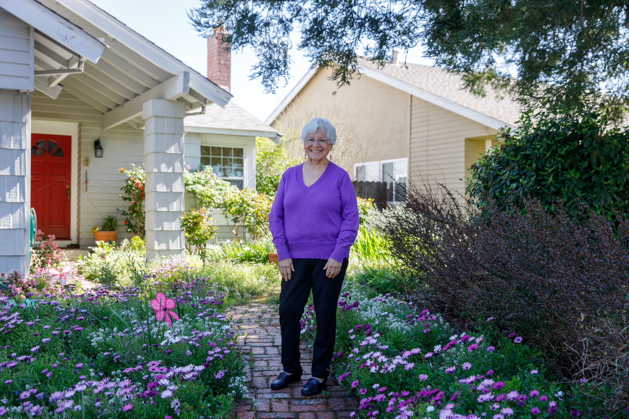 Betty Labastida stands in her gorgeous flower garden in Napa, Calif. She is an older Latina woman with a welcoming smile, white hair and a colorful purple sweater that matches the abundant wildflowers in her front yard.