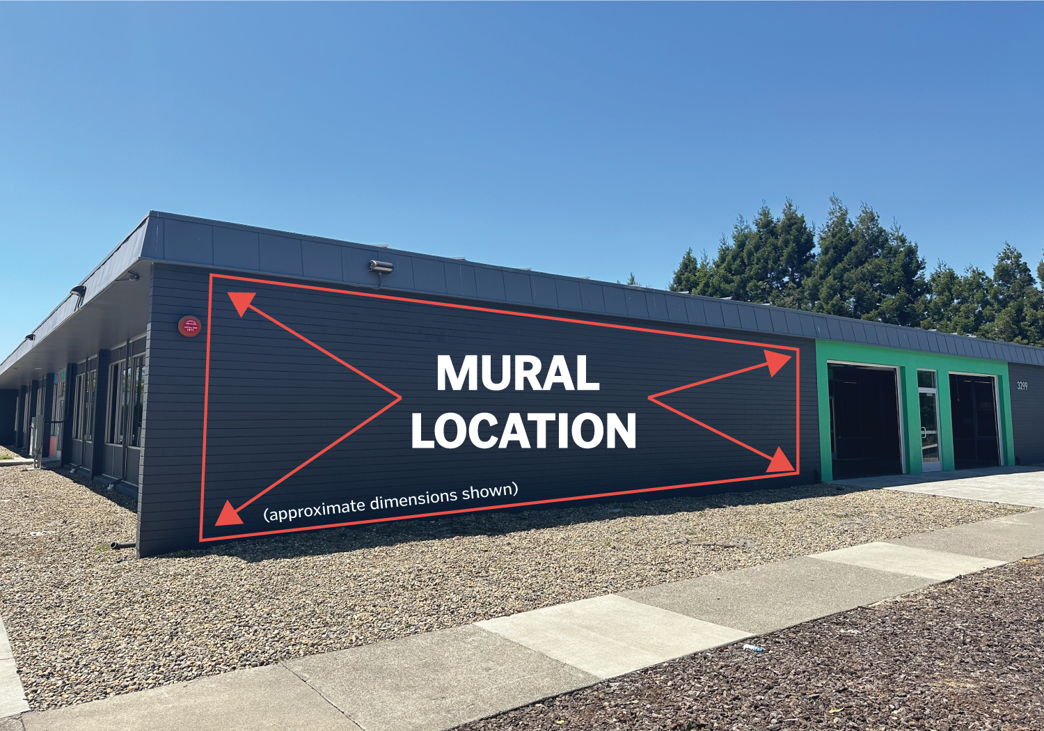 A photo of NVCF's building showing the southeastern facade. It is a single story building, painted grey, with a large empty wall perfect for a mural. The Open wall area is marked with arrows and text that reads MURAL LOCATION